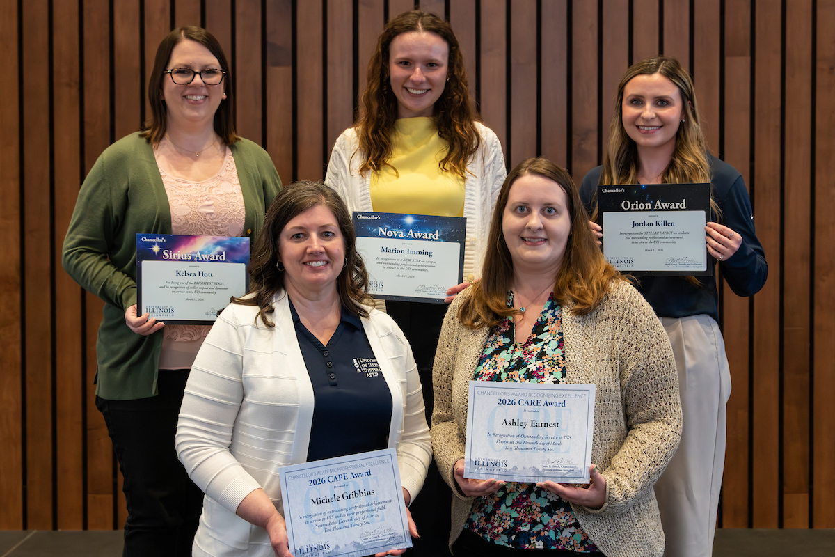 Five employees recognized with annual staff awards stand in two lines, smiling, holding their award certificates.