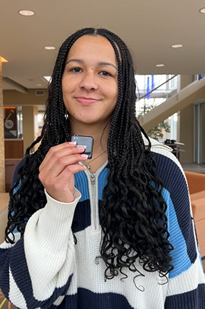 Young person with long hair holding a small object, smiling indoors.