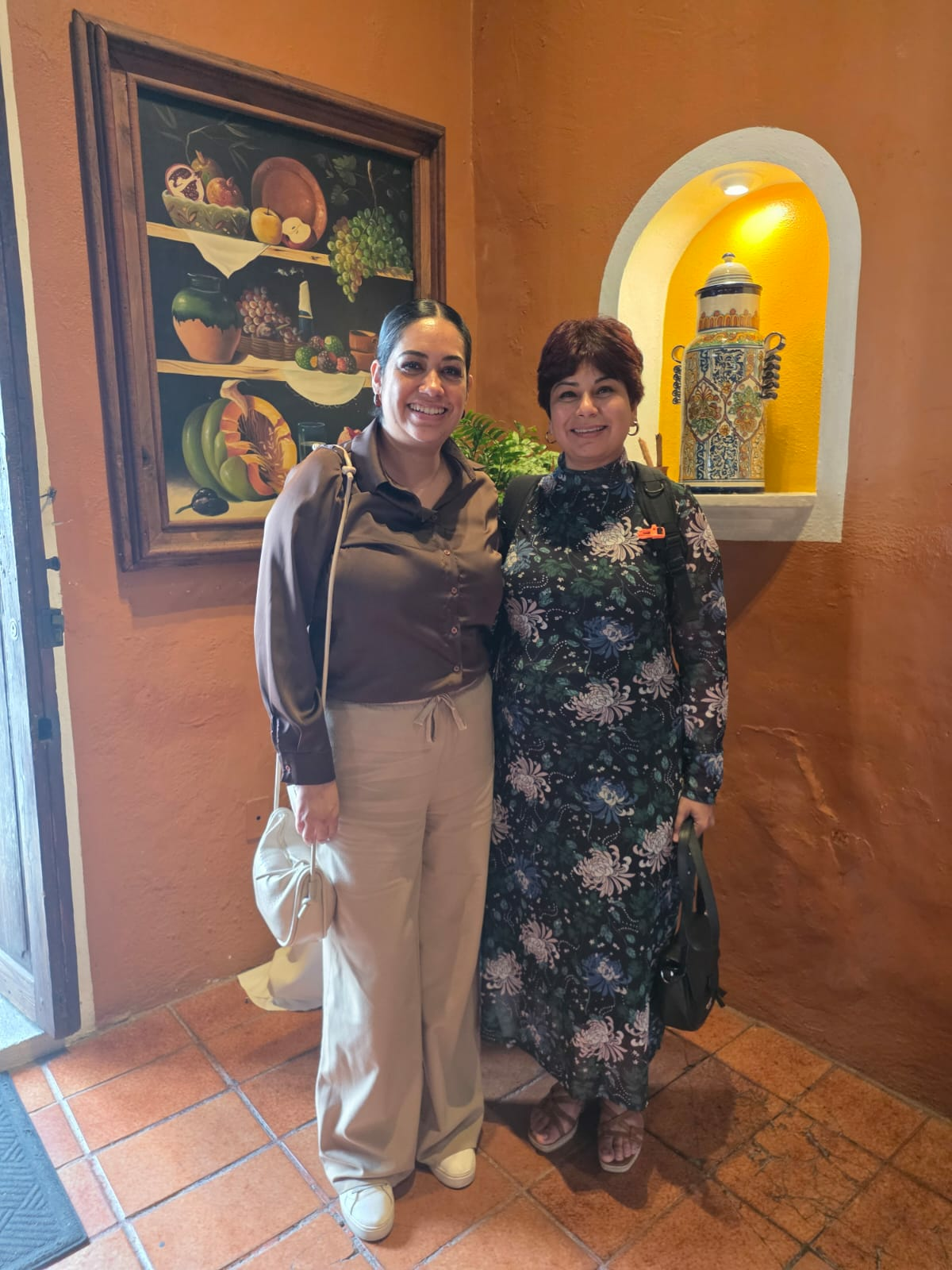 Shipra Gupta and a colleague pose inside a restaurant with colorful artwork and decorative pottery.