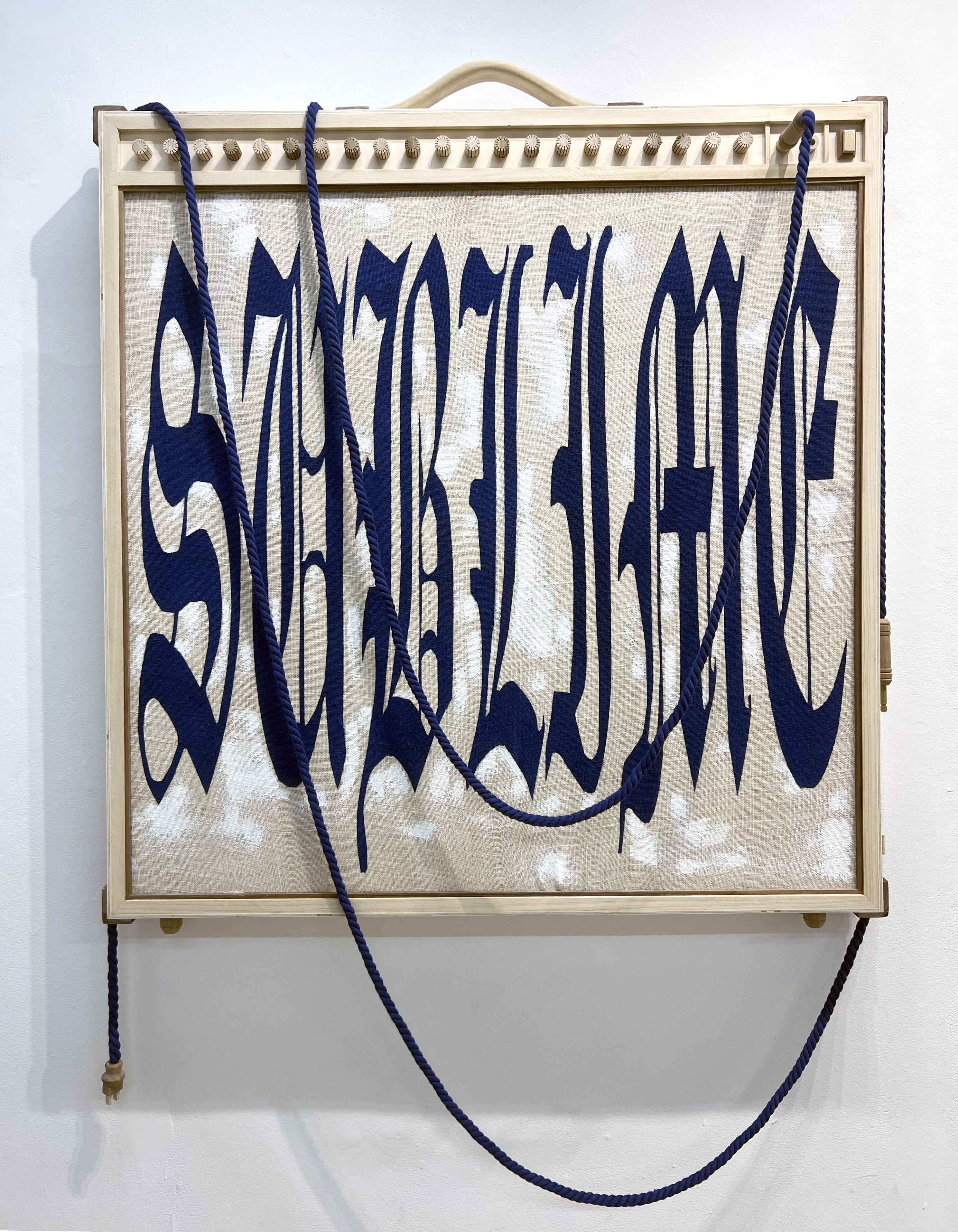 Mixed-media sculpture by Mike Rea with elongated blue lettering spelling “Sublime” on fabric, framed in wood and intertwined with blue rope.
