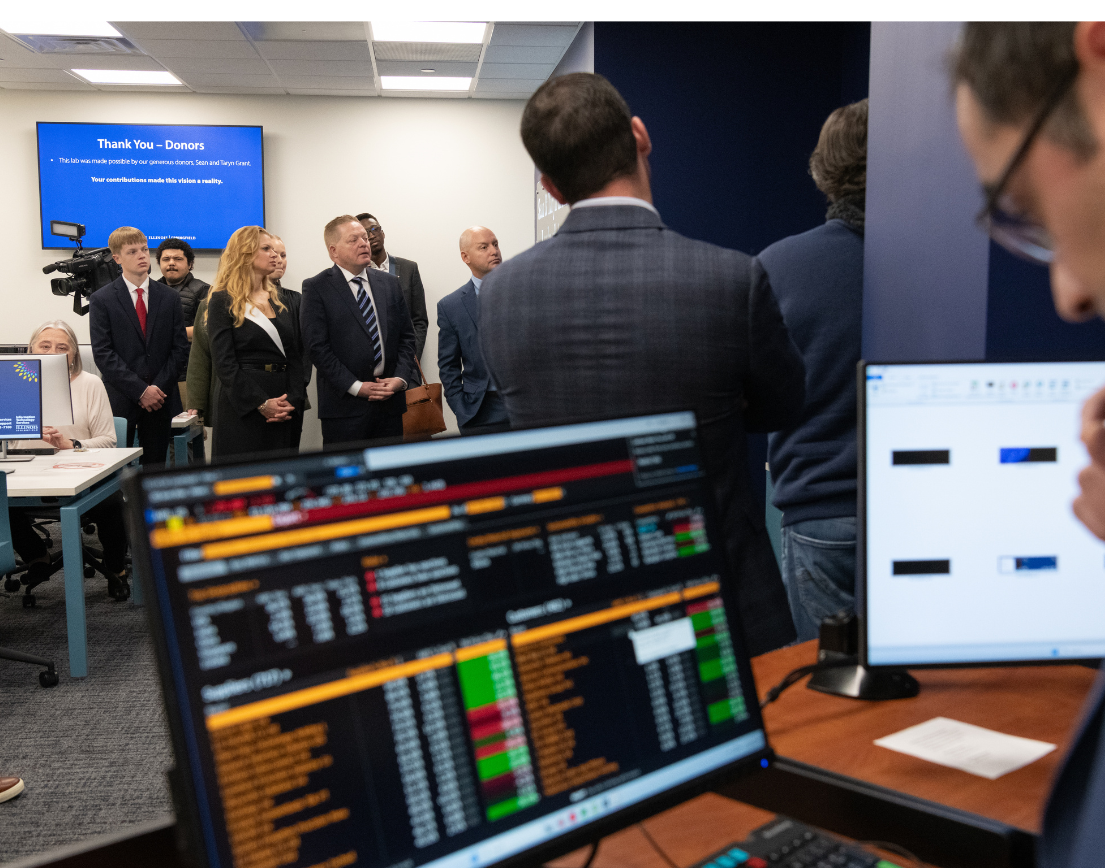 A computer screen full of data, with people in suits in the background.