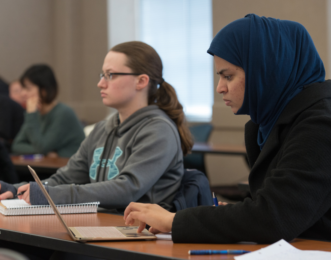 A student in a headscarf focusing on their computer.