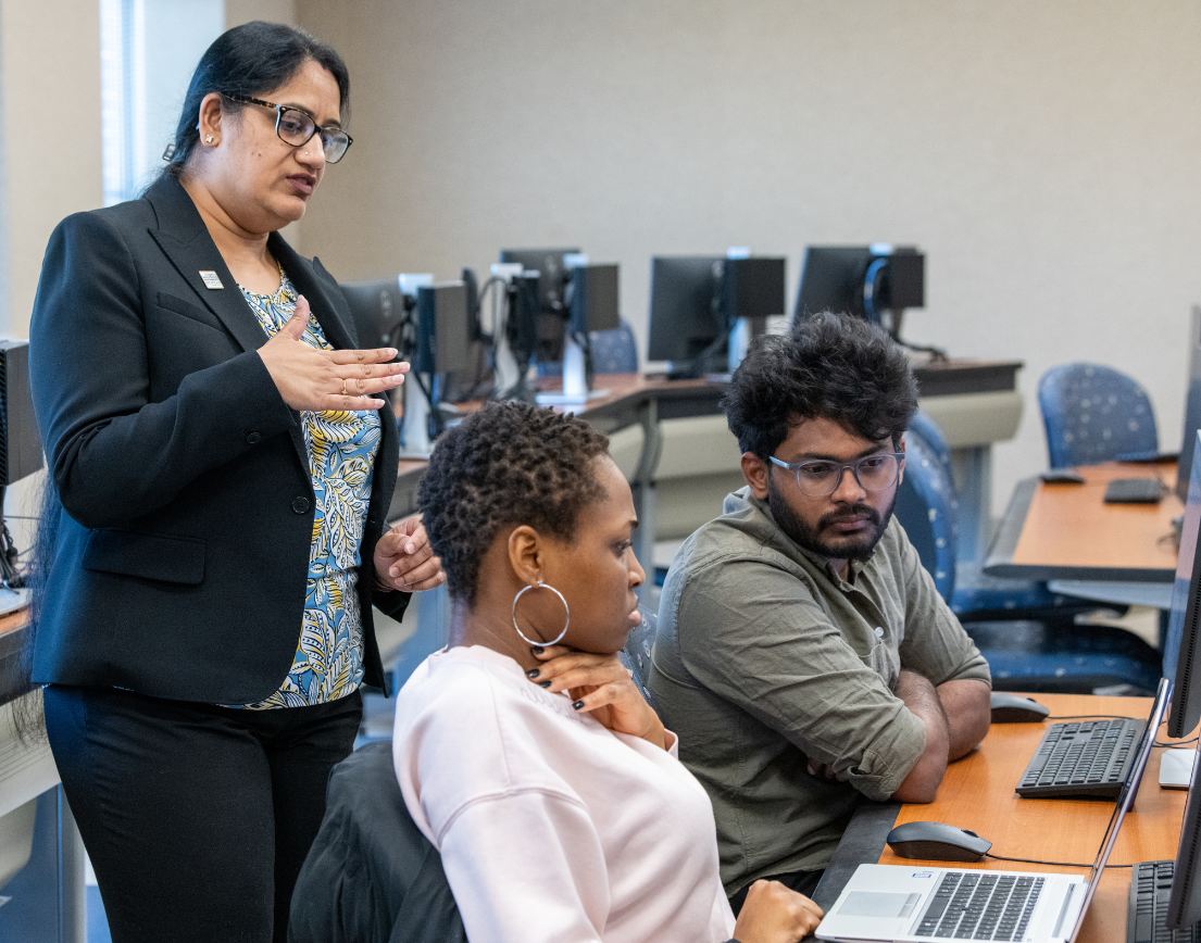 A teacher teaching two students at their computers.