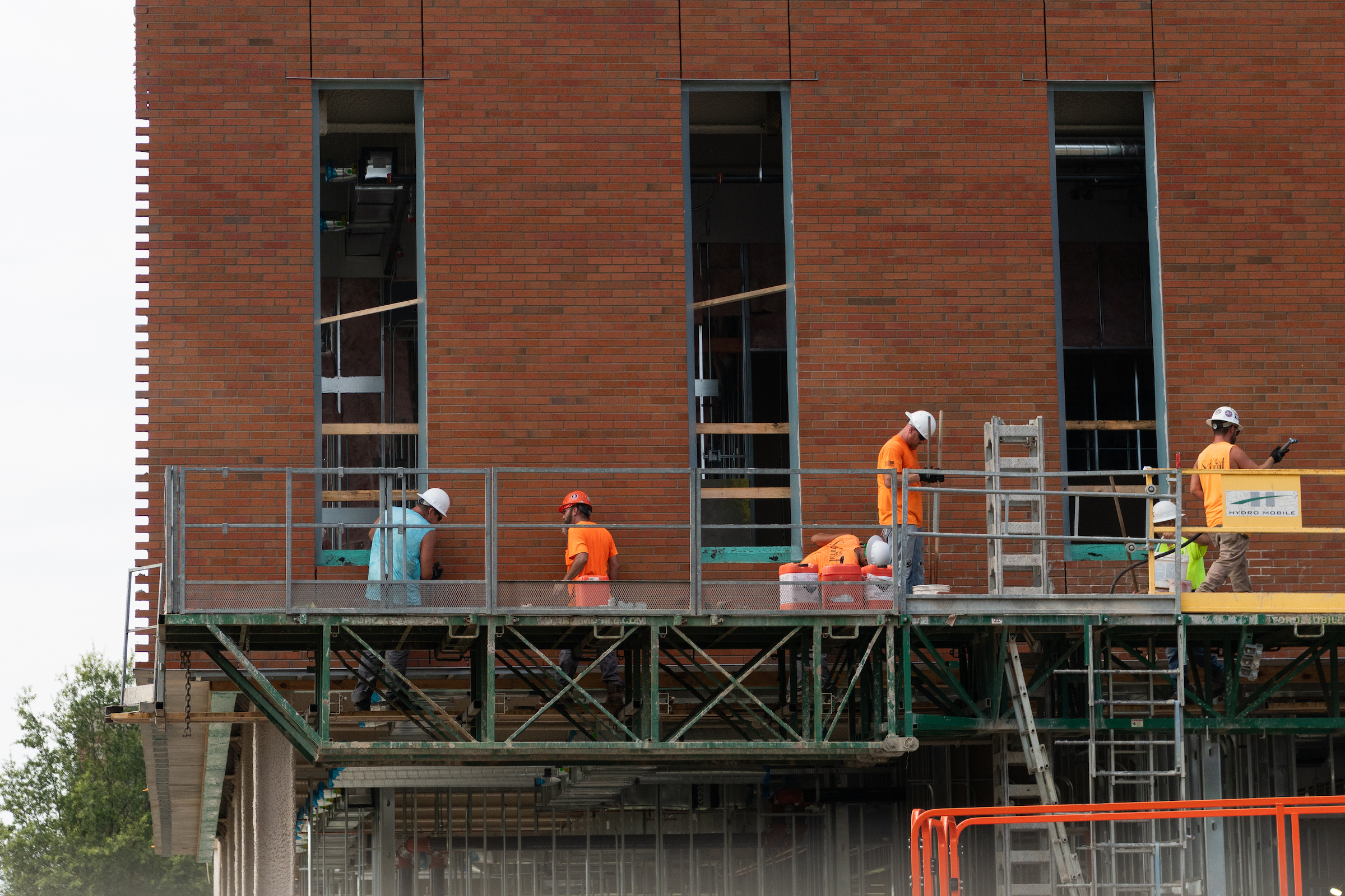 Construction workers install brickwork on the exterior of the UIS Library Commons from elevated scaffolding.