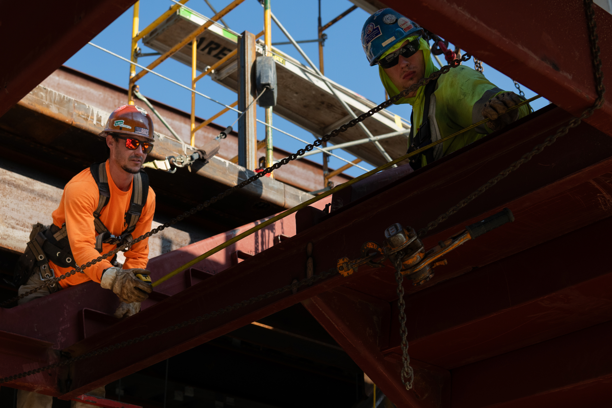 Two construction workers measure and work on structural steel beams at the UIS Library Commons construction site.