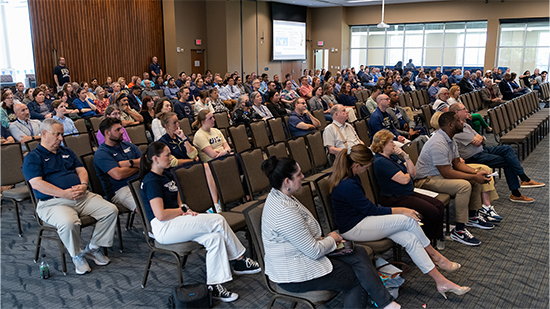 Audience seated in a large conference room, attentively watching a presentation.