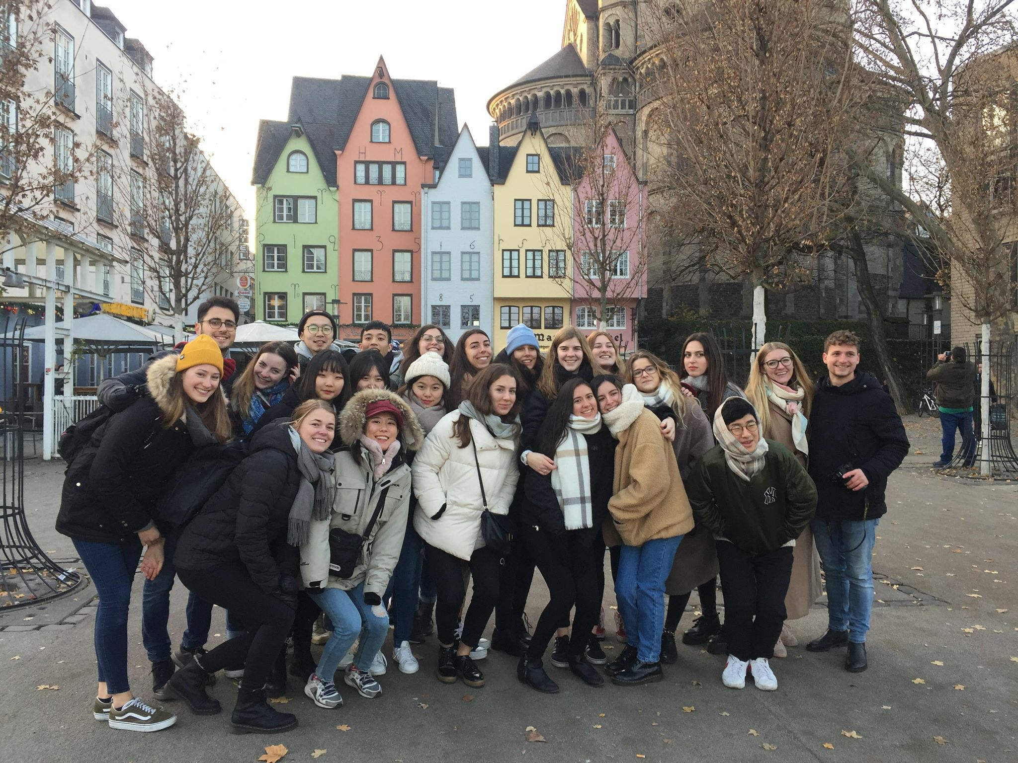 25 Erasmus/Exchange students outside in the winter/fall standing in front of pastel-colored buildings