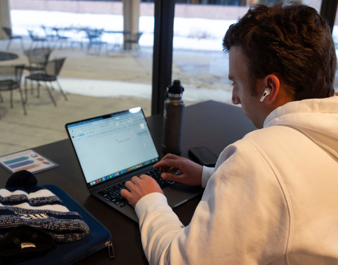 Student in white hoodie looking at computer outside at a table. 