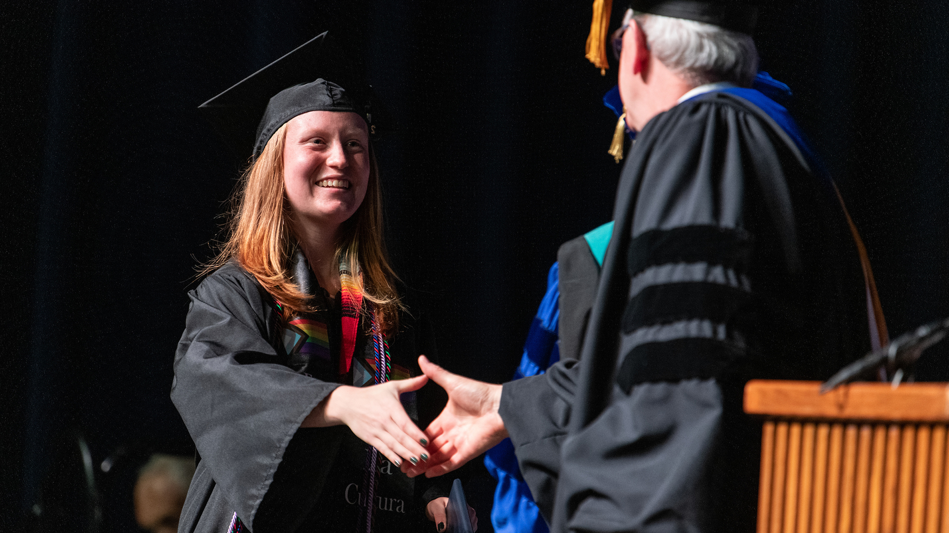 A UIS student in cap and gown shakes hands on the Commencement stage.