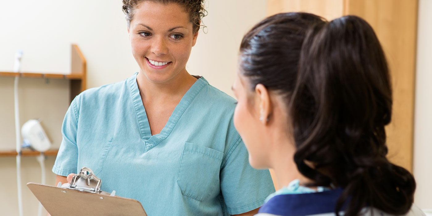 Two people talking. One in scrubs holding clipboard.