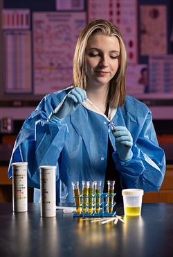 An MLS student wearing a blue lab coat suctions a liquid from a vial.