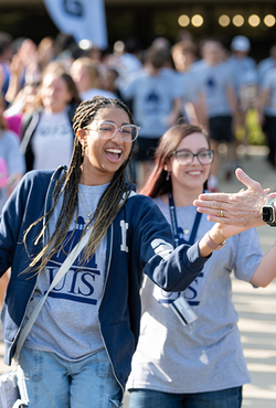 Two students smile while slapping the extended hands of faculty and staff at Convocation.