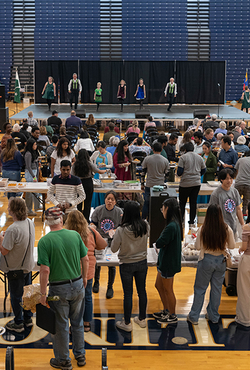 People line up for food as performances take place on stage.