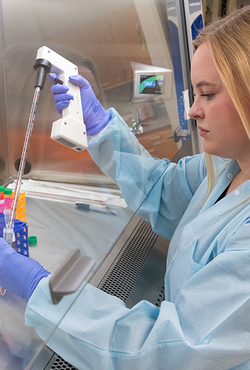 Student in a lab coat and gloves using a pipette for research in a sterile lab environment.