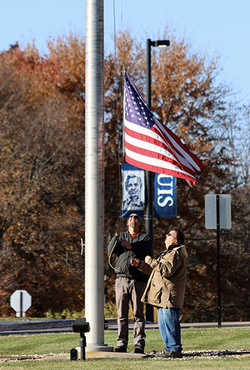 Two veterans raise a flag up a pole.