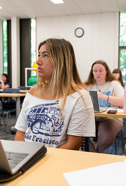 Students attentively listen in a classroom, taking notes and using laptops during a lecture at the University of Illinois Springfield.