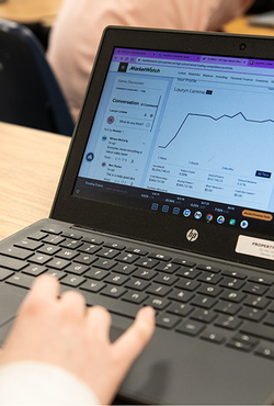 A laptop with stock trading information on the screen sitting on a desk with a person's hand above the mousepad. 