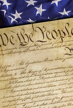 Close-up of the United States Constitution with the words “We the People” visible, placed over an American flag background.