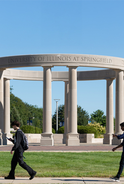 Two students walk in front of the UIS colonnade on a sunny day.