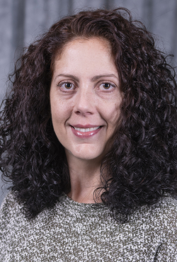 Smiling woman with curly hair against a gray backdrop.