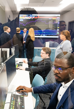 People working at computers in an office with a stock market screen.