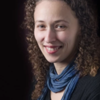 Yona Stamatis with curly hair and blue scarf on a dark background.