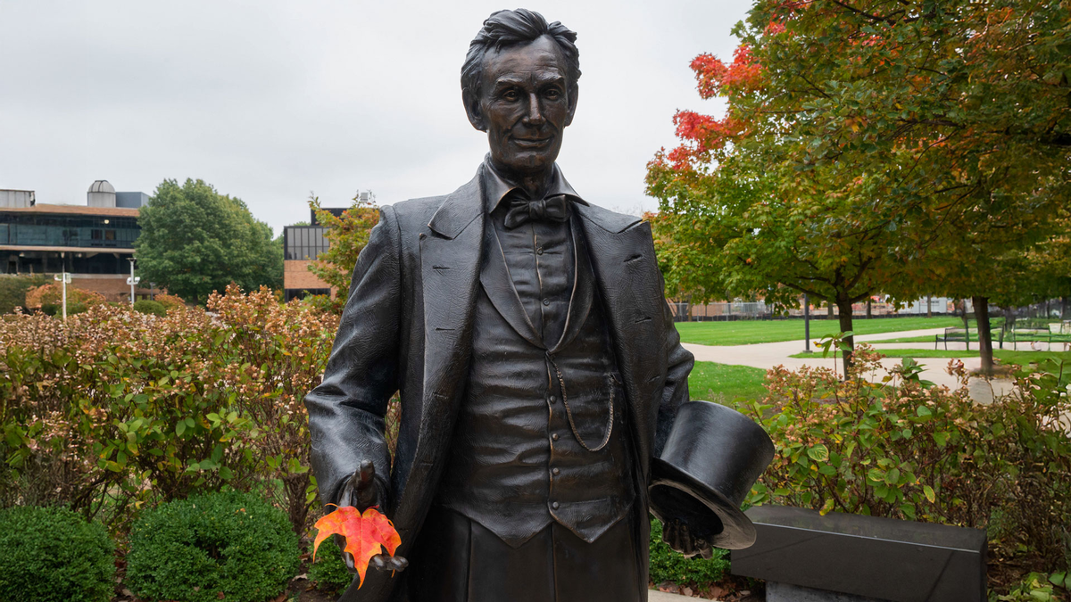 the lincoln statue on campus holding an orange autumn leaf in his hand