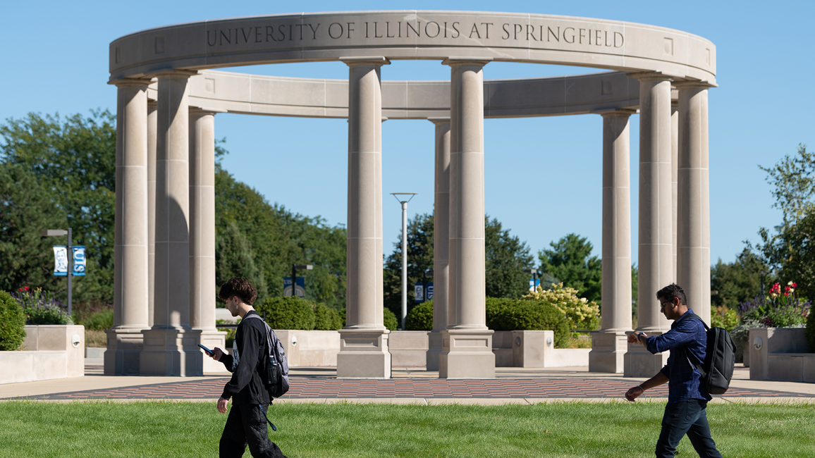 Two students walk in front of the UIS colonnade on a sunny day.