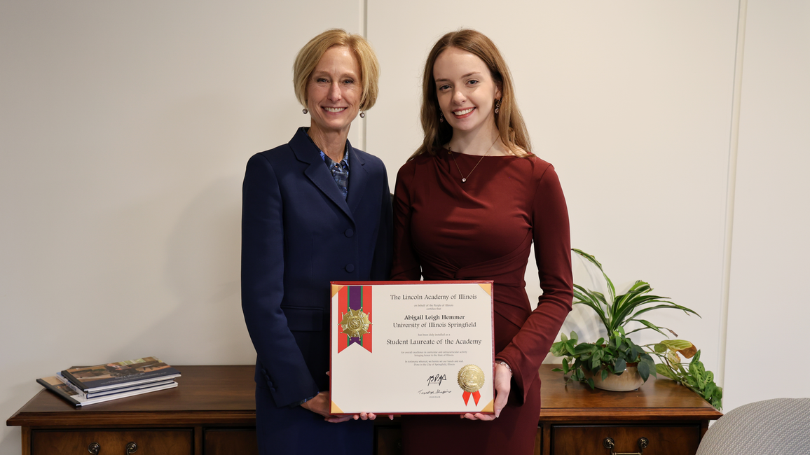 Two women smiling, holding a certificate in a dimly lit room.