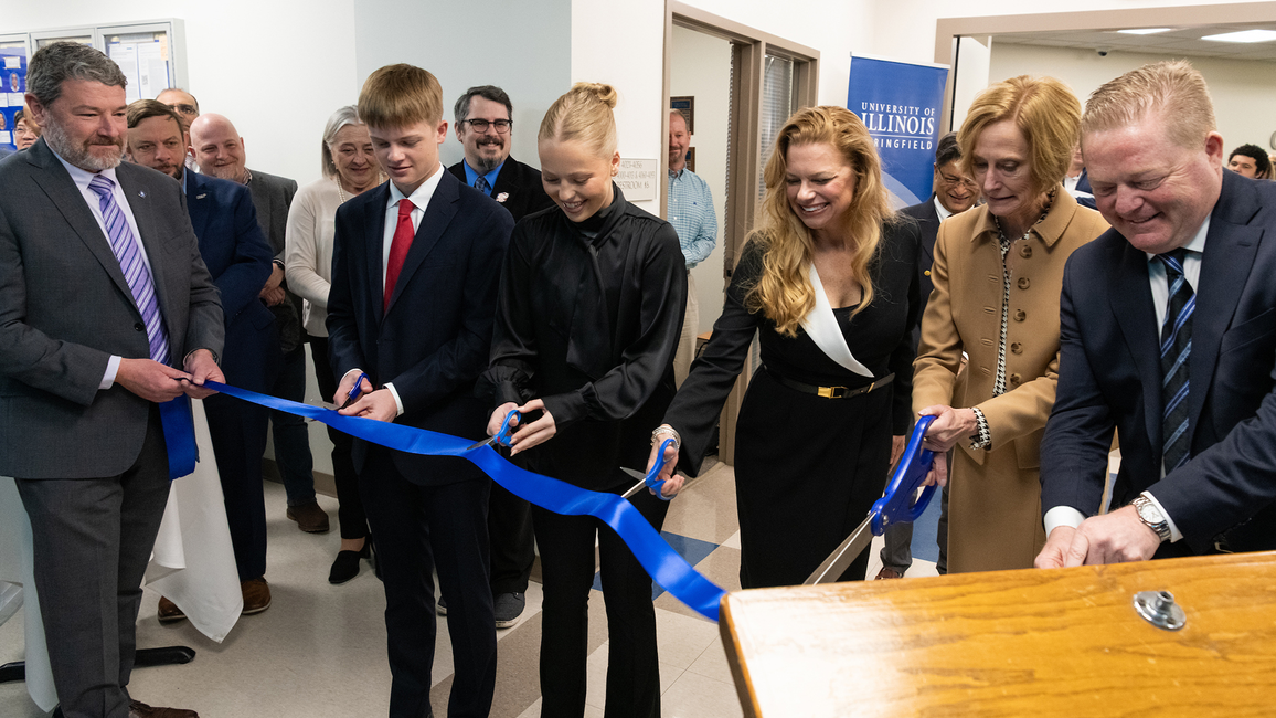 A group of people cutting a blue ribbon at an indoor event.