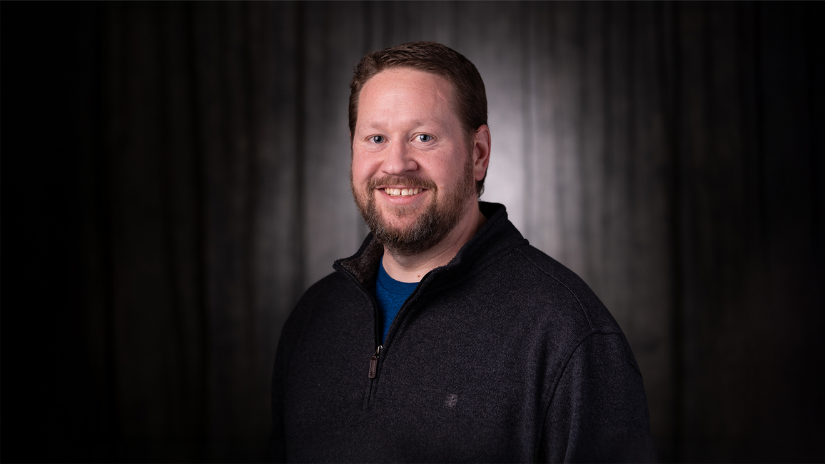 Jeff Sudduth, a smiling man in dark sweater against a dark background.
