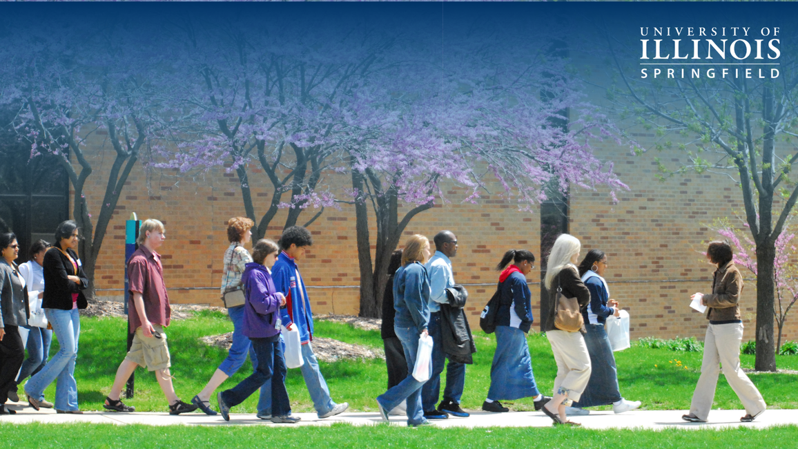 Students walking on a campus path with blooming trees around them.