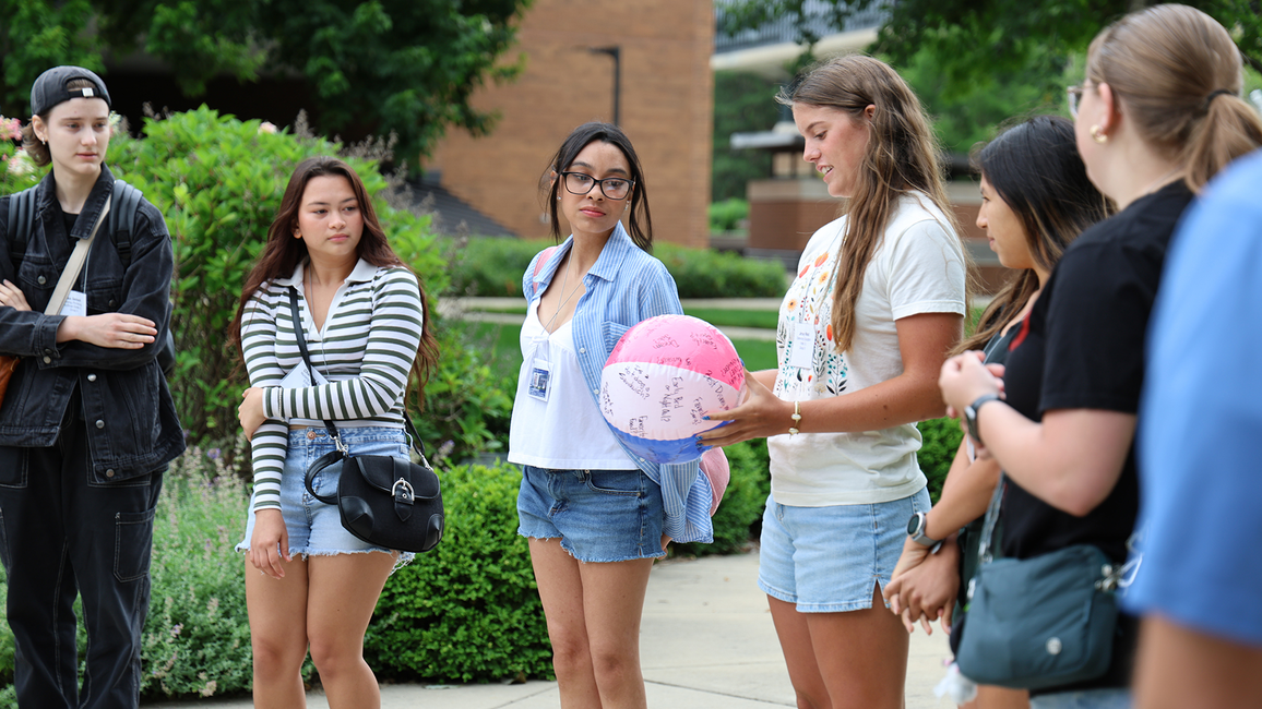 Group of people outdoors, one holding a beach ball, listening intently.