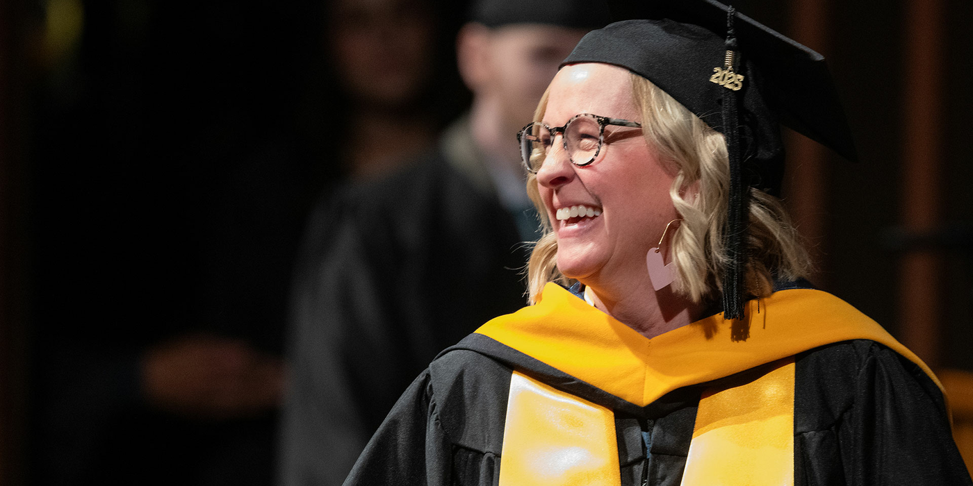 Smiling graduate in cap and gown with gold stole.