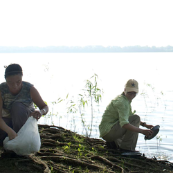 two people cleaning up garbage near a lake