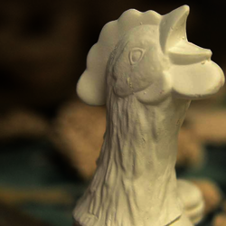 Ceramic rooster head with other ceramic works in the background.