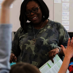 a teacher in the middle of a classroom with lots of raised hands