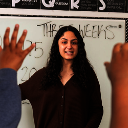 a teacher in the middle of a classroom with lots of raised hands