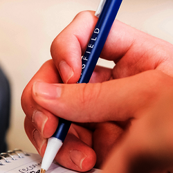 closeup image of a hand writing with a blue UIS pen