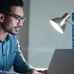 Man coding at night, illuminated by screen and lamp.