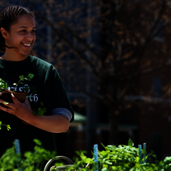 a student holding a plant while standing behind a table filled with other plants