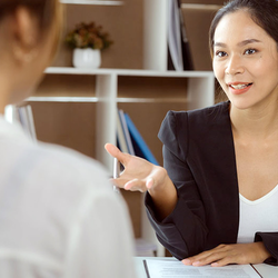 Businesswoman in a black blazer talking to another person in an office setting.
