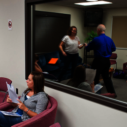 People sitting in a waiting room with red chairs and paintings on the wall.