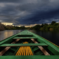 View out of the front of a green boat onto the Amazon river under dramatic skies