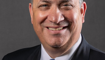 Professional portrait of Athletic Director Mike Hermann wearing a blue tie and dark suit.