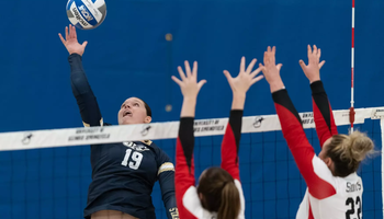 Makenna Cox seen through the net as Saints go up for a block