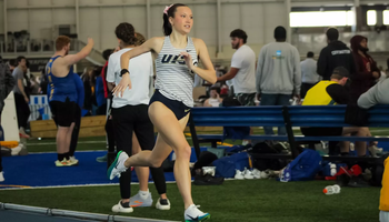 Madelyn Miller-Ross running indoor track in white UIS uniform
