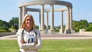 Alyssa Hasler poses in front of UIS Colonnade in gold volleyball uniform
