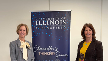 Two women standing beside University of Illinois Springfield banner indoors.