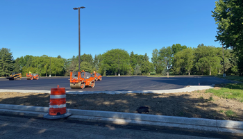 Paved parking lot under clear blue sky, surrounded by trees, with orange construction cones.